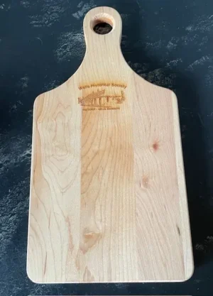 Wooden cheeseboard with a rounded handle and an engraved Wells Historical Society depot design.