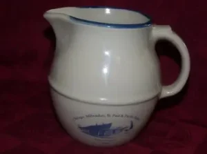 Cream Red Wing pitcher with a blue rim and a blue illustration of the Wells depot.