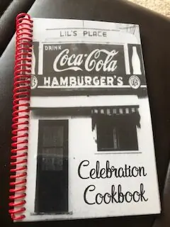 Celebration Cookbook with red spiral binding and a black-and-white photograph of Lil's Place on the cover.