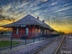 Wells Depot Museum beside railroad tracks under a blue and golden evening sky.