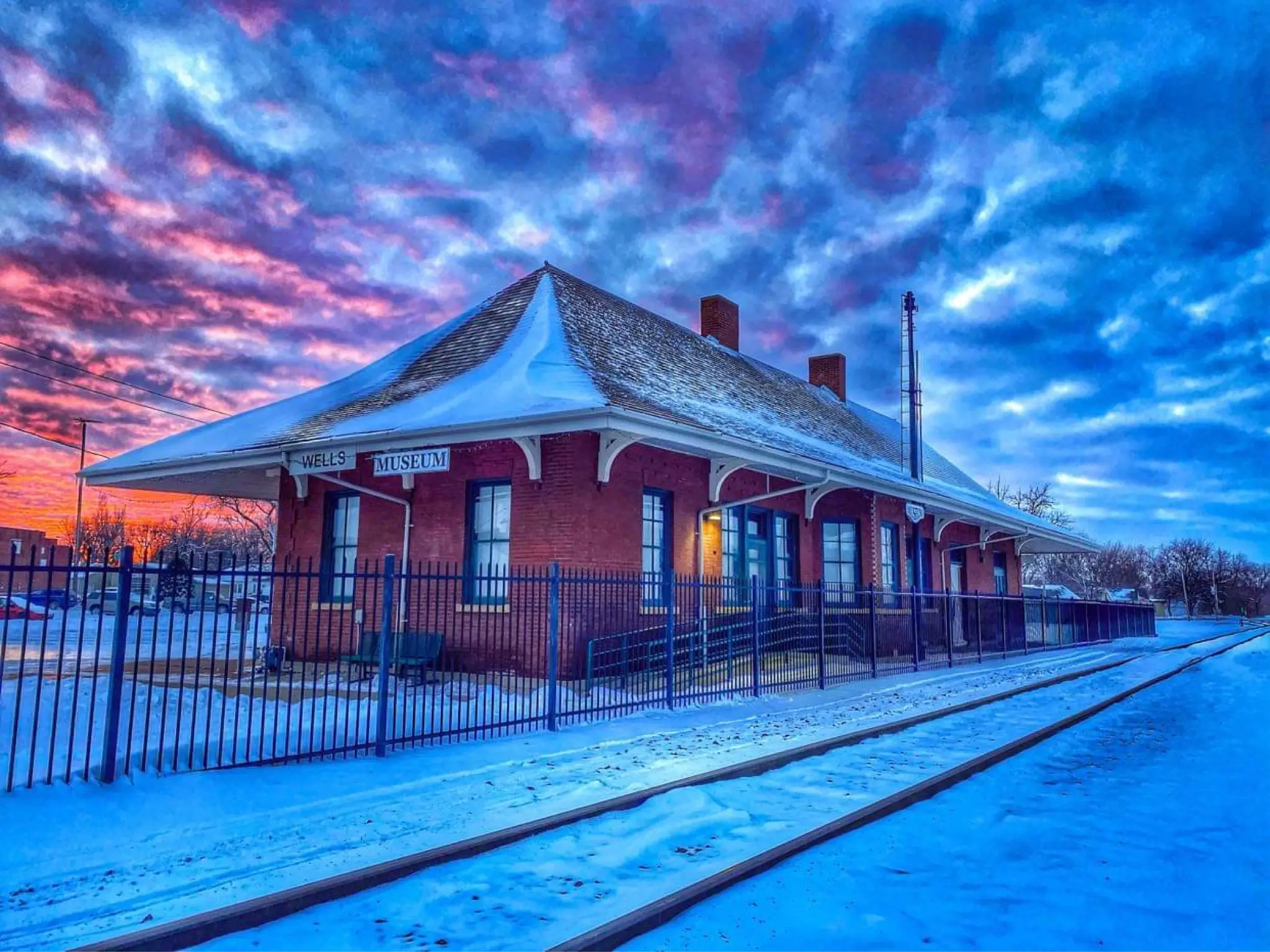 Wells Depot Museum and railroad tracks covered in snow beneath a pink and blue winter sky.