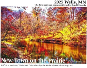 2025 Wells calendar cover showing autumn trees reflected in a stream, titled New Town on the Prairie.